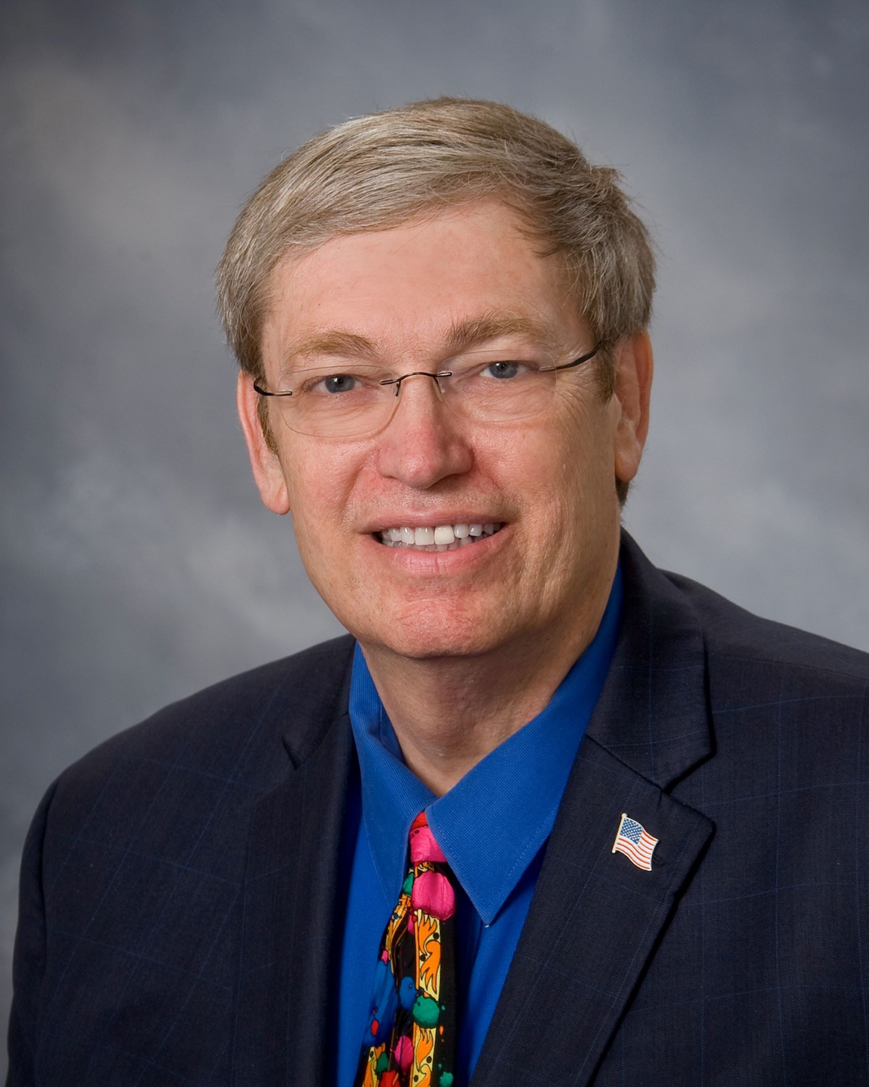 Bio Photo of Don Cole wearing blue suit, blue shirt and tie with American flag lapel pin